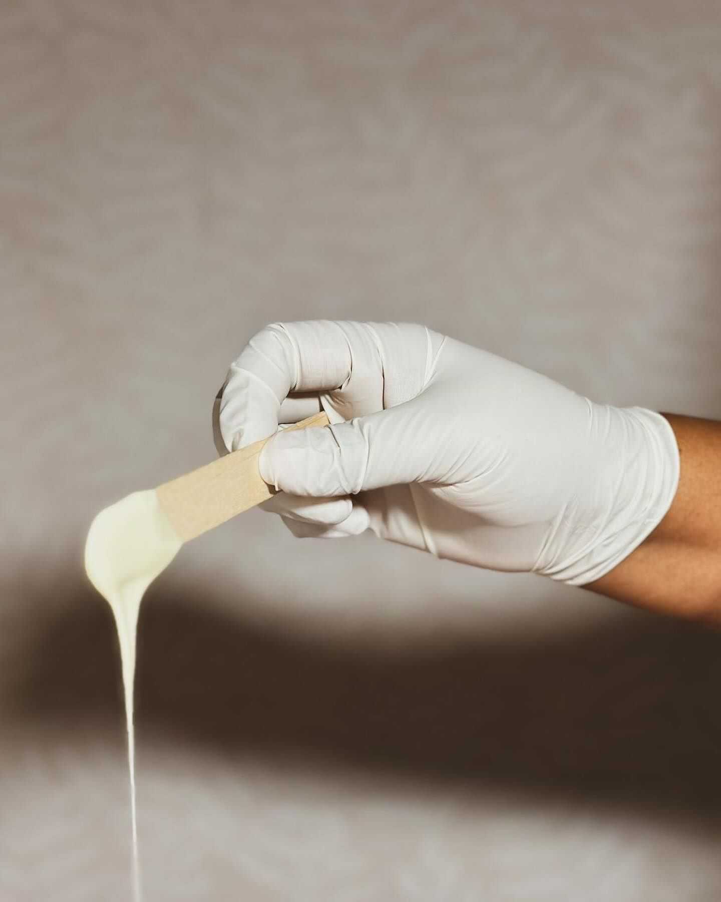 Gloved hand holding a stick with liquid wax dripping off for waxing treatment.