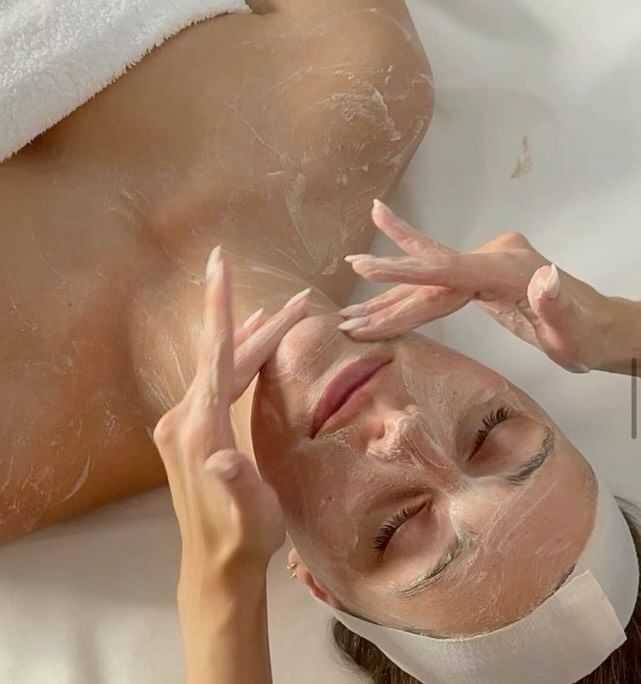 Woman receiving a facial treatment with a white towel draped over her shoulders.