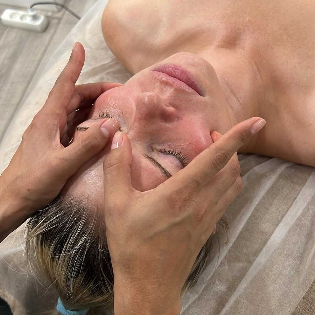 Person receiving a facial massage while lying down on a treatment table.
